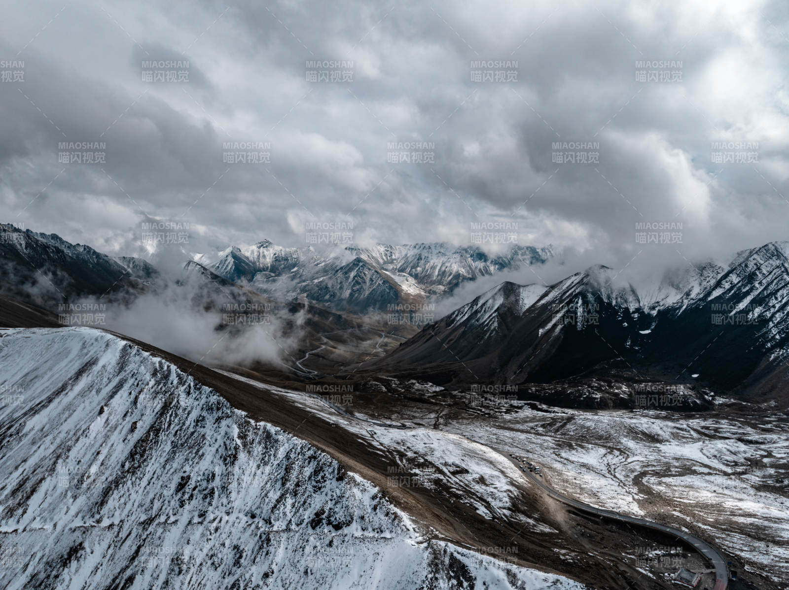 雪山云雾缭绕下蜿蜒道路点缀的高山壮丽景观图片