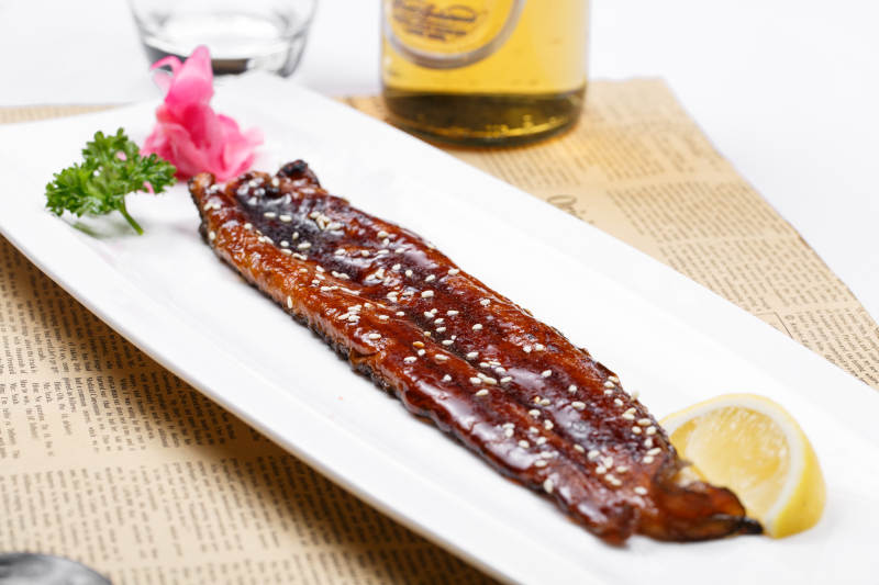 长方形瓷盘装的日式烤鳗鱼摆放在英文包装纸上图片