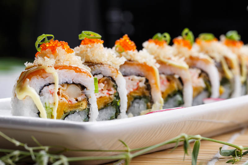 长瓷盘装的蟹籽教授卷摆放在寿司帘上图片