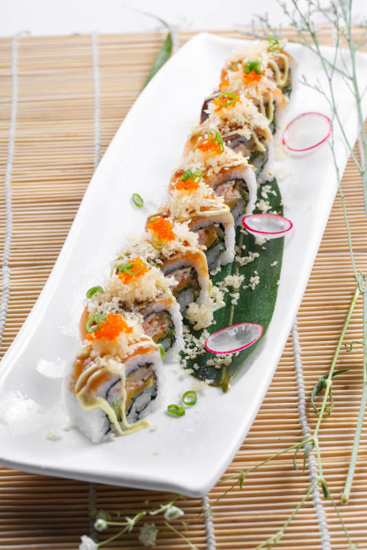 长瓷盘装的蟹籽教授卷摆放在寿司帘上图片