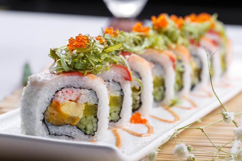 长瓷盘装的蟹籽教授卷摆放在寿司帘上图片