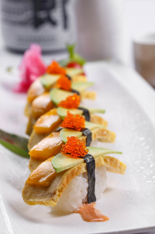 烧蛋蟹子芒果手握寿司摆放在寿司帘上图片