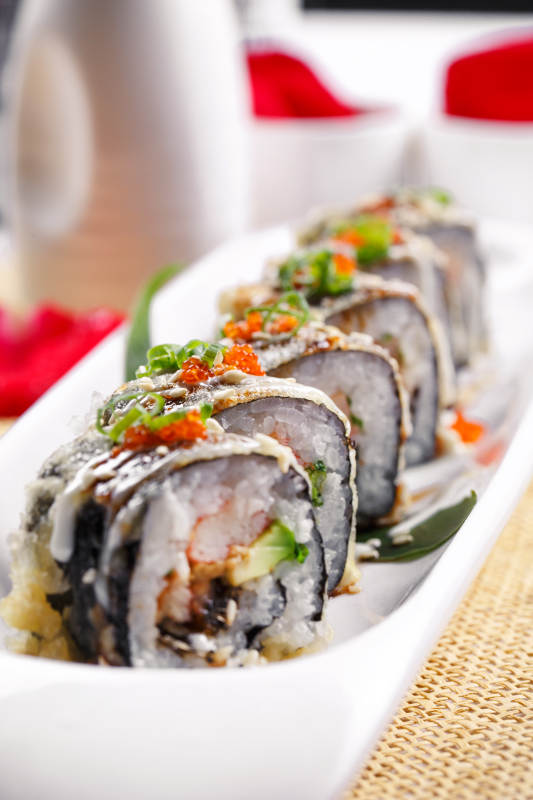 椭圆长瓷盘装的鹅肝手卷寿司摆放在草垫上图片