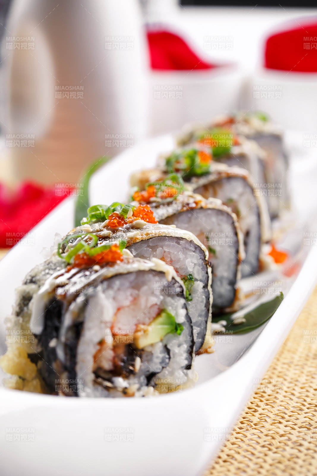 椭圆长瓷盘装的鹅肝手卷寿司摆放在草垫上图片