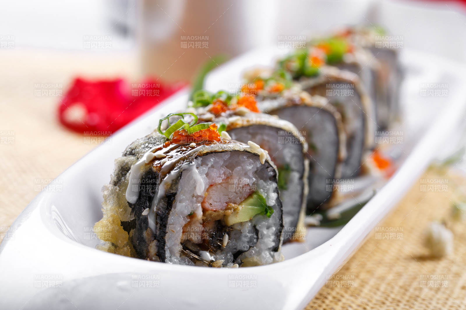 椭圆长瓷盘装的鹅肝手卷寿司摆放在草垫上图片