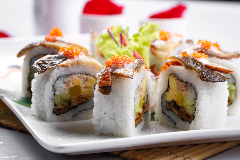 什锦鳗鱼手卷寿司摆放在寿司帘上图片