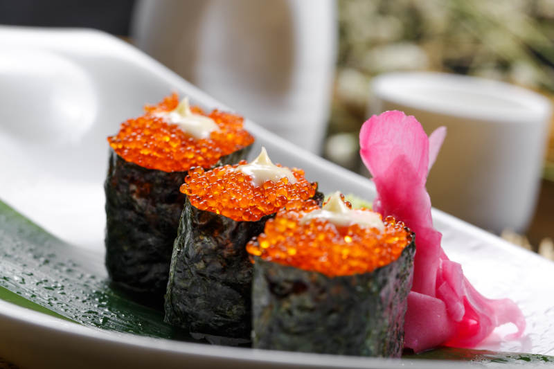 鹅颈瓷盘装的蟹子军舰手握寿司摆放在石头上图片