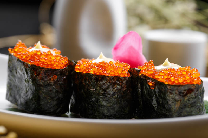 鹅颈瓷盘装的蟹子军舰手握寿司摆放在石头上图片