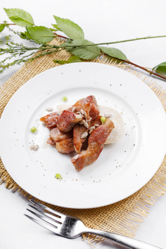 圆形白瓷盘装的铁板煎牛腹肉摆放在草垫上图片