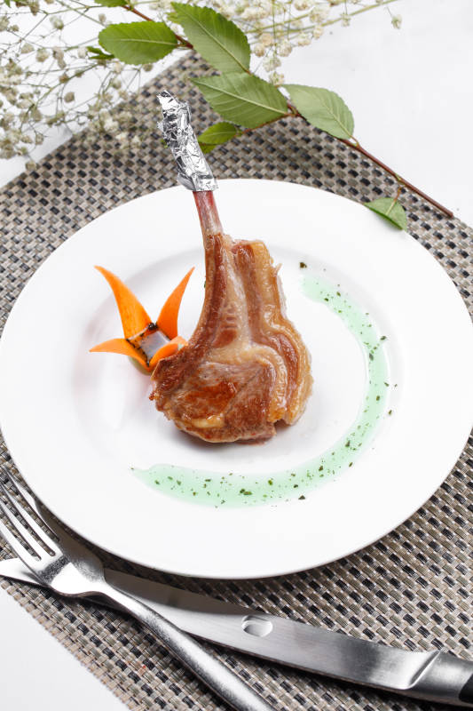 圆形白瓷盘装的波尔多法式铁板羊排摆放在餐垫上图片