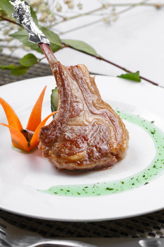 圆形白瓷盘装的波尔多法式铁板羊排摆放在餐垫上图片