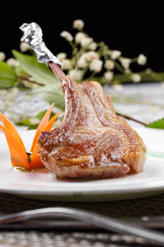 圆形白瓷盘装的波尔多法式铁板羊排摆放在餐垫上图片