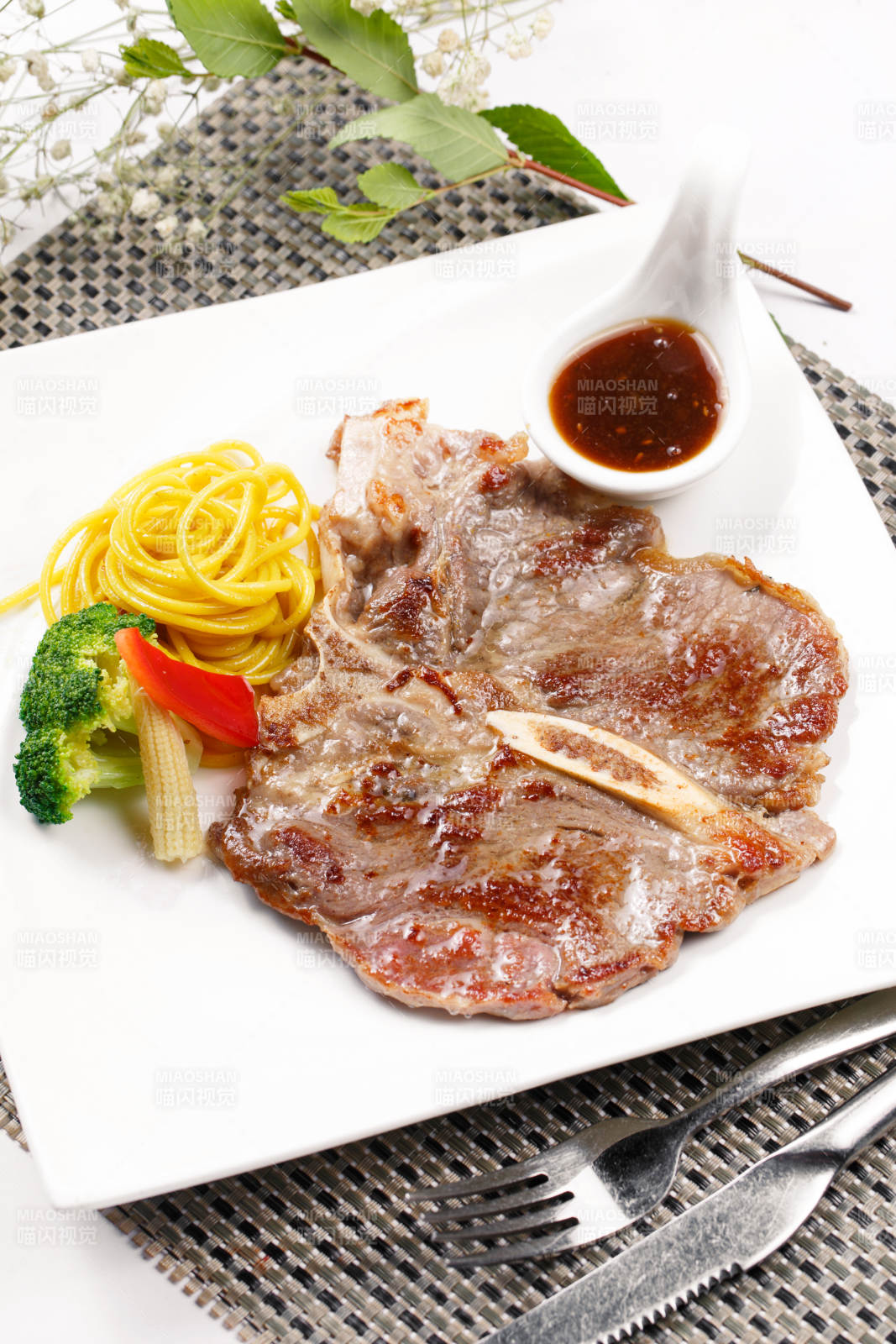 方形瓷盘装的新西兰T骨牛排摆放在餐垫上图片