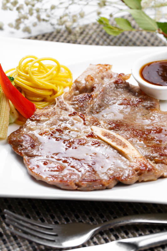 方形瓷盘装的新西兰T骨牛排摆放在餐垫上图片