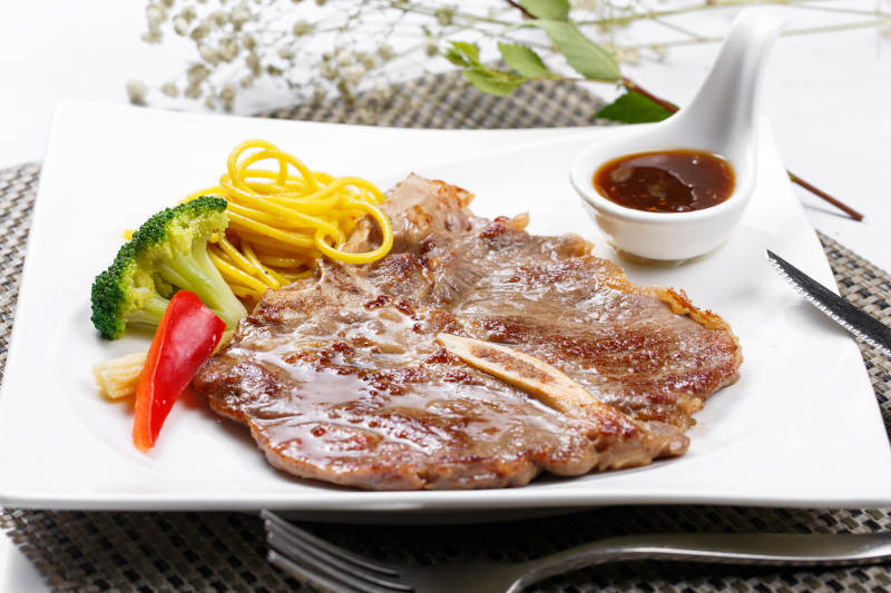 方形瓷盘装的新西兰T骨牛排摆放在餐垫上图片