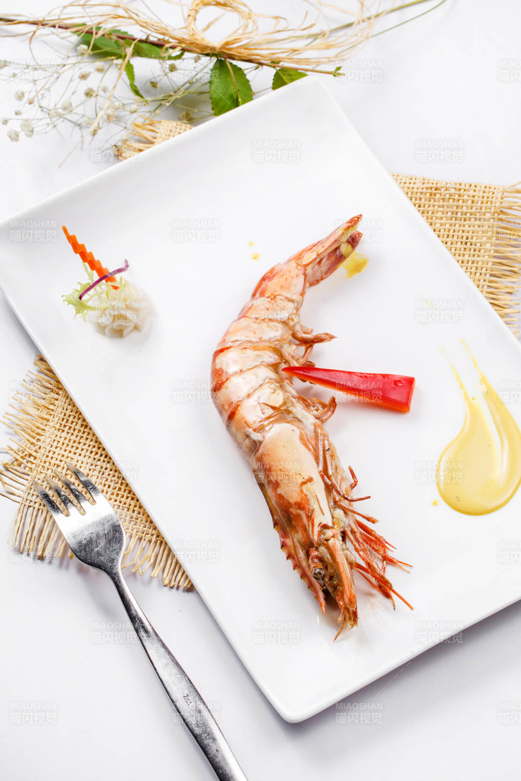 长方形瓷盘装的铁板野生明虾皇摆放在草垫上图片
