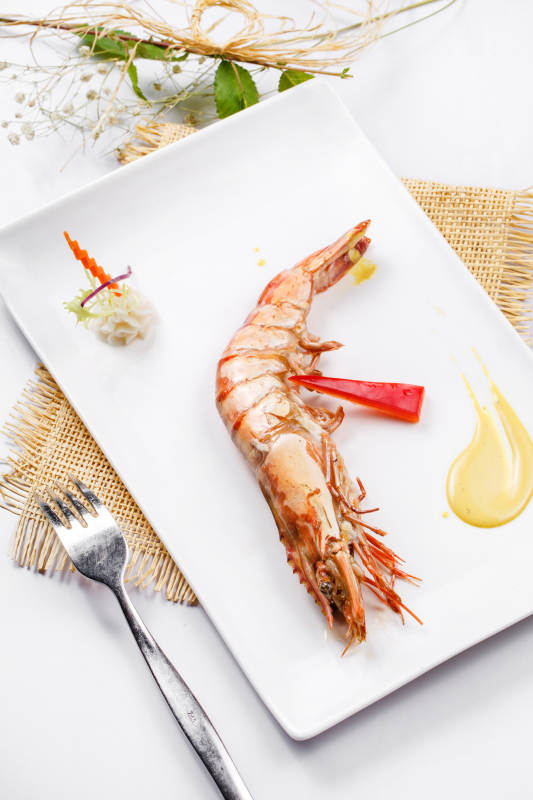 长方形瓷盘装的铁板野生明虾皇摆放在草垫上图片