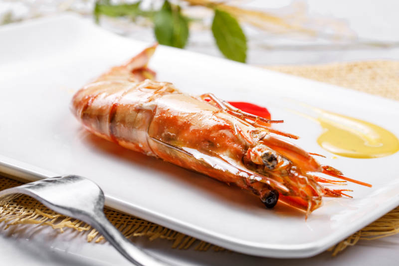 长方形瓷盘装的铁板野生明虾皇摆放在草垫上图片