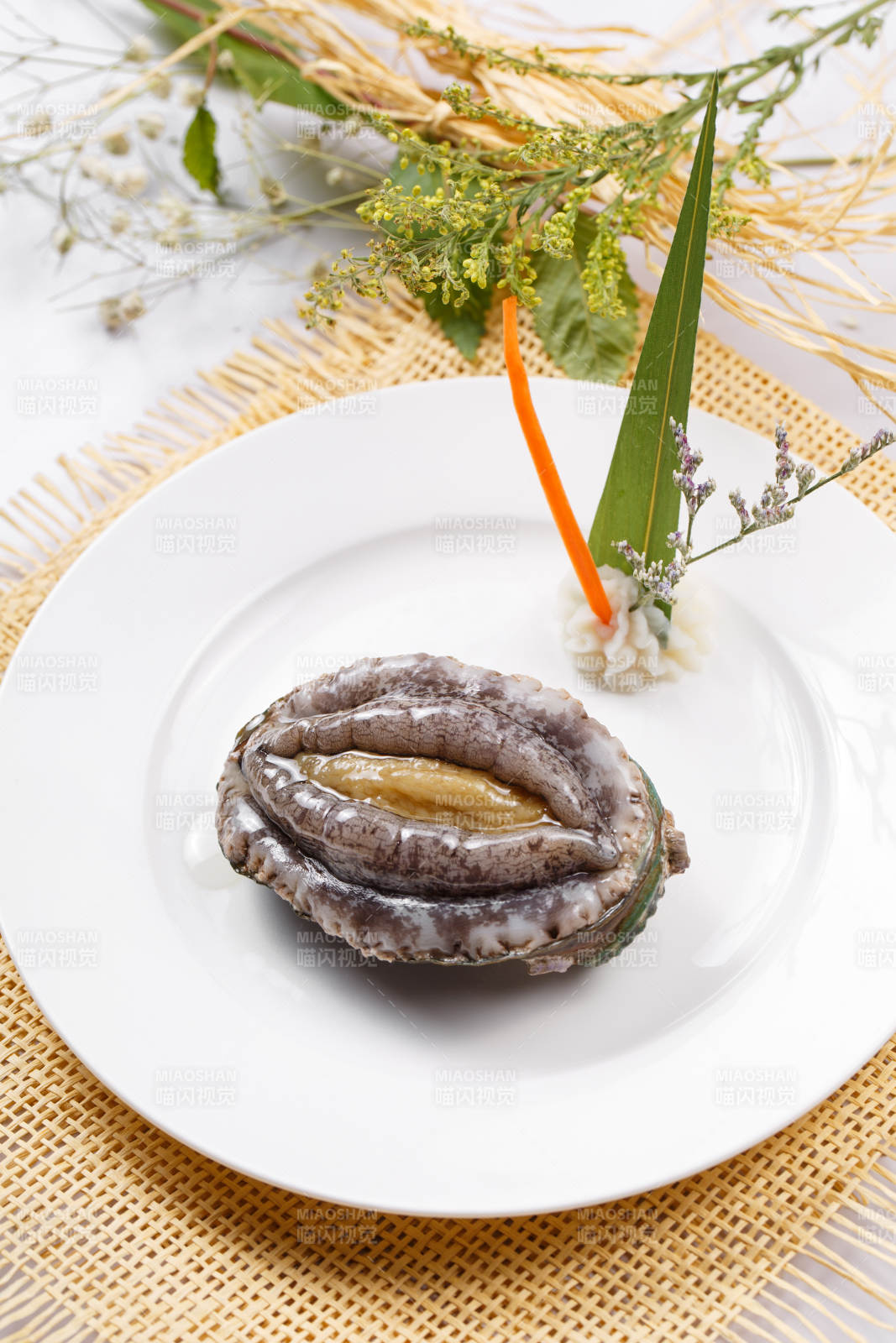 圆形瓷盘装的生鲜活鲍鱼摆放在草垫上图片
