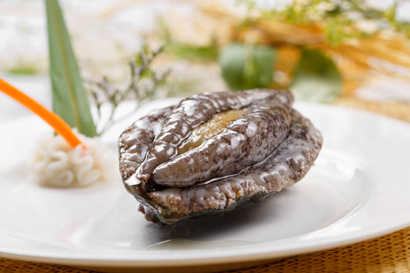 圆形瓷盘装的生鲜活鲍鱼摆放在草垫上图片