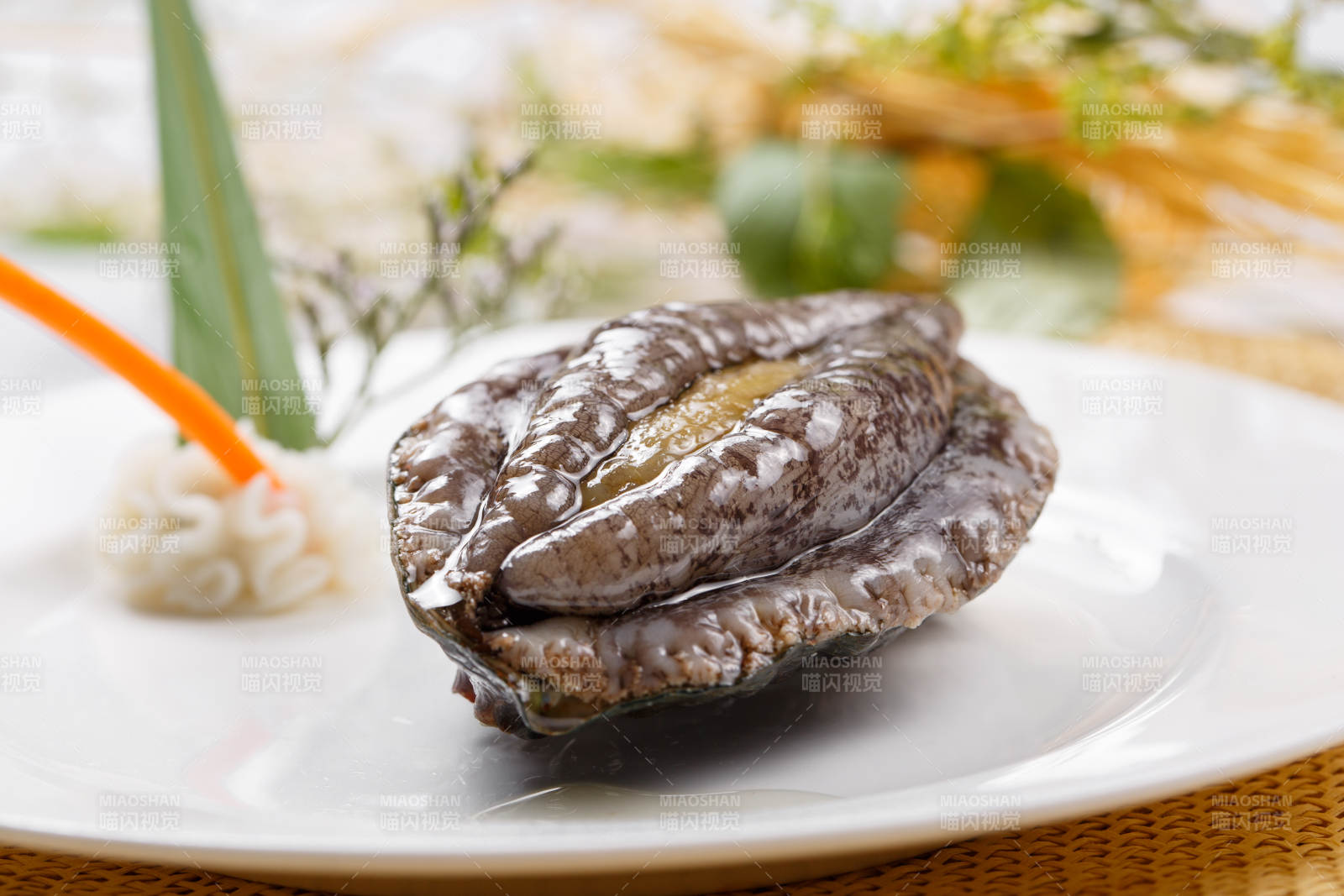 圆形瓷盘装的生鲜活鲍鱼摆放在草垫上图片