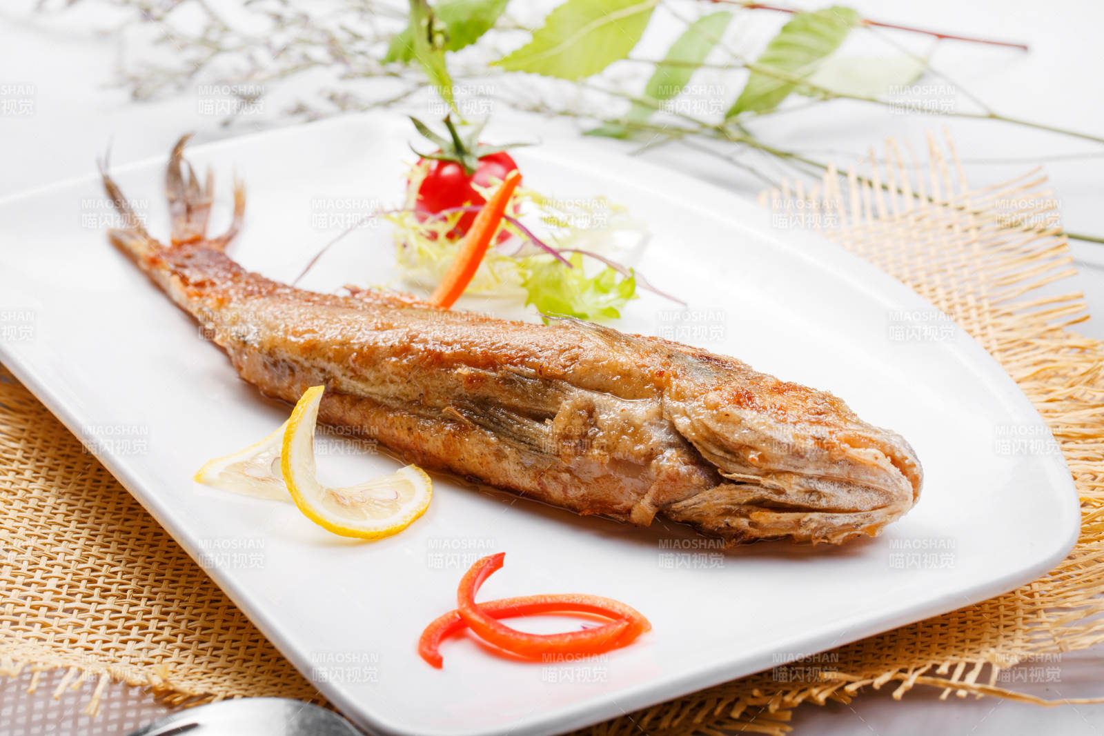 方形瓷盘装的日式铁板煎黄花鱼摆放在草垫上图片