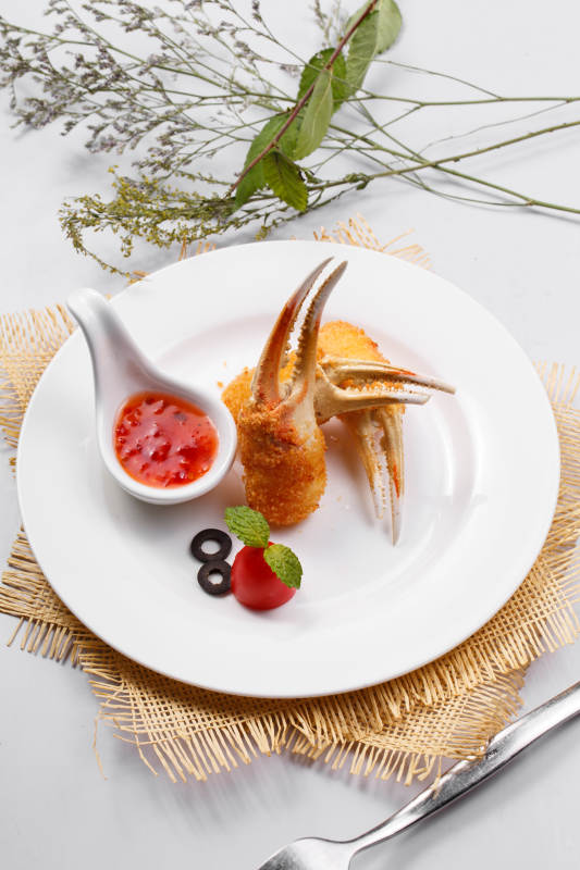 白色圆盘装面包糠芝士焗梭蟹钳摆放在草垫上图片