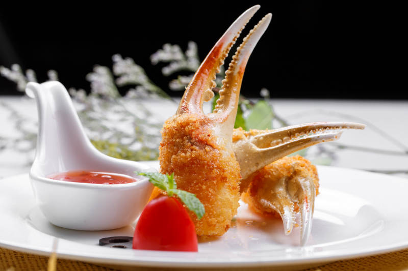 白色圆盘装面包糠芝士焗梭蟹钳摆放在草垫上图片