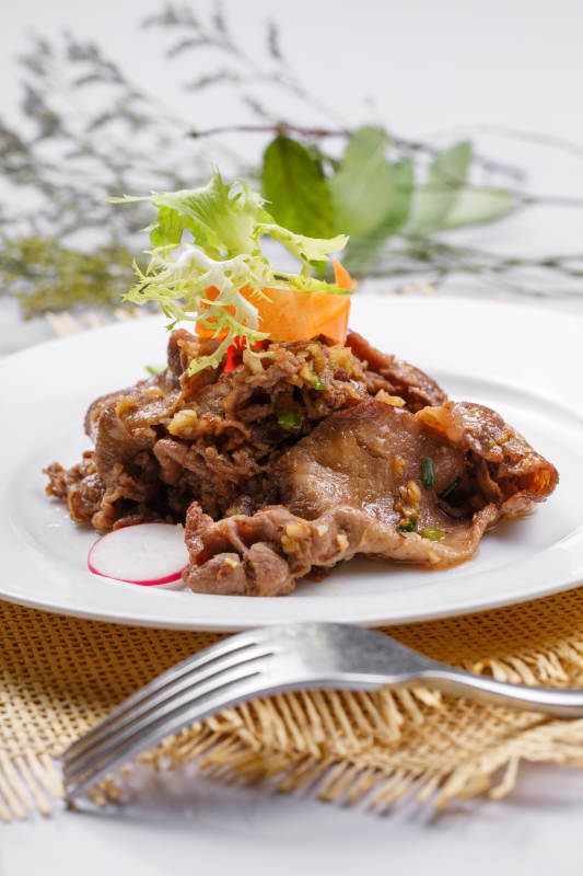 圆形白瓷盘装的铁板蒜香牛舌摆放在草垫上图片