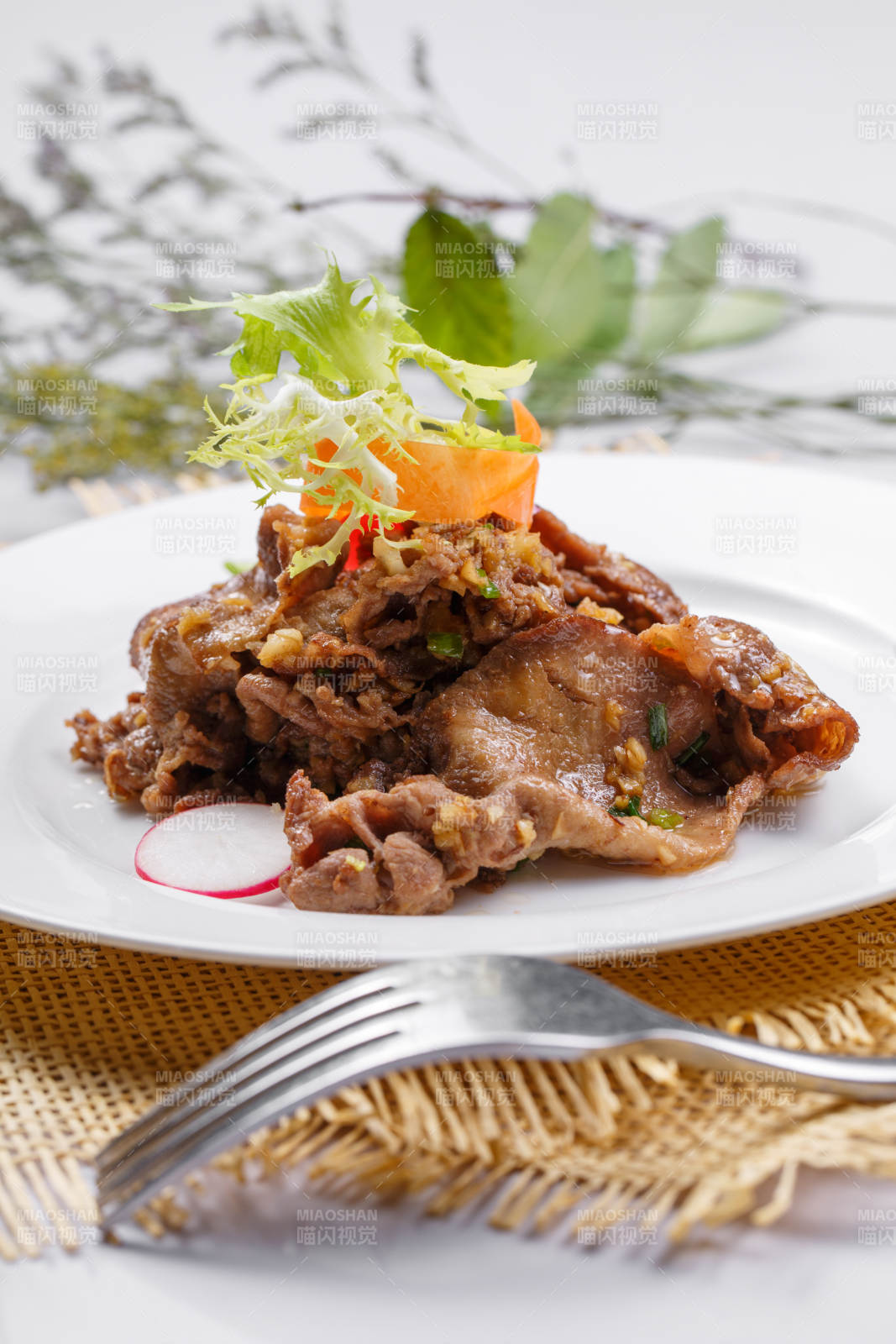 圆形白瓷盘装的铁板蒜香牛舌摆放在草垫上图片