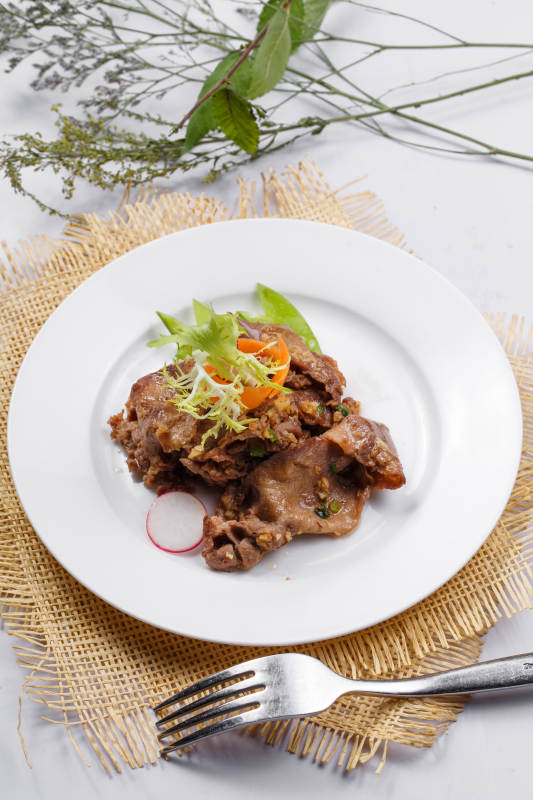 圆形白瓷盘装的铁板蒜香牛舌摆放在草垫上图片