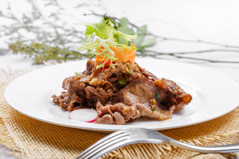 圆形白瓷盘装的铁板蒜香牛舌摆放在草垫上图片