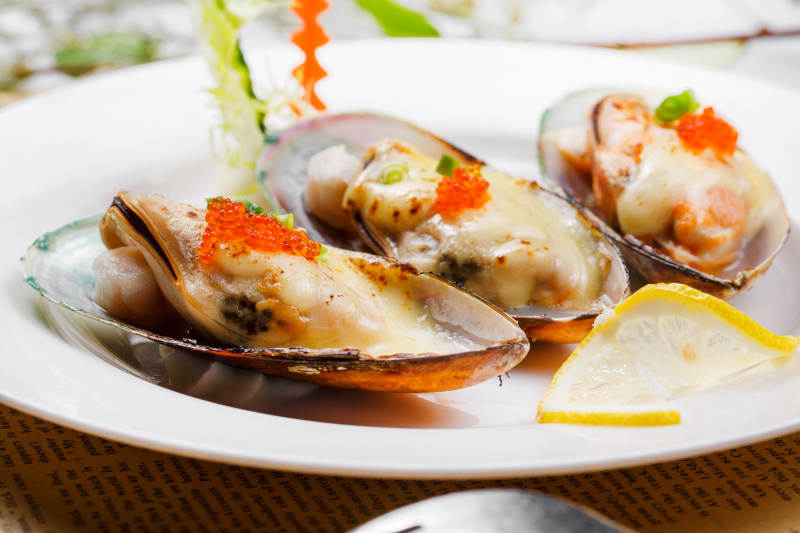 圆形瓷盘装的马苏里拉芝士焗青口贝贻贝摆放在英文包装纸上图片