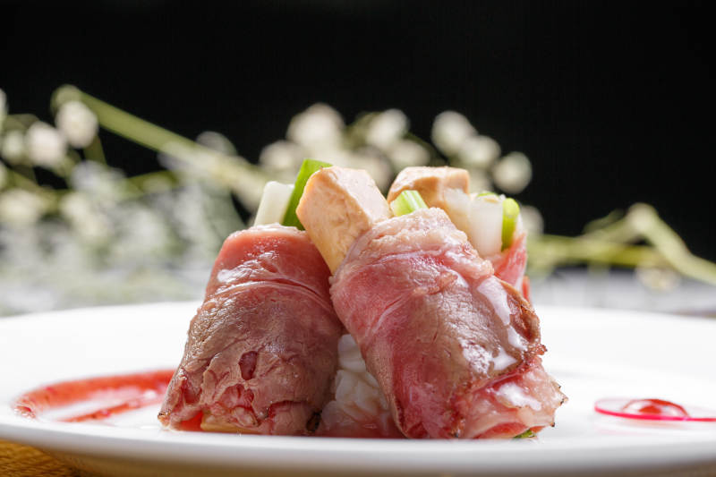 白色圆盘装的法式鹅肝牛肉卷摆放在草垫上图片