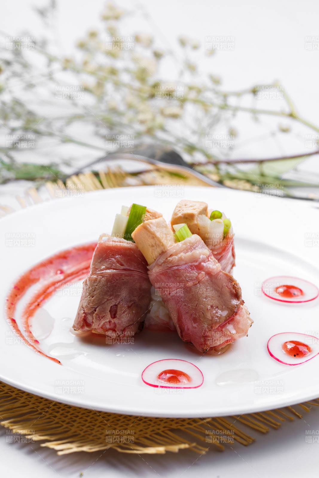 白色圆盘装的法式鹅肝牛肉卷摆放在草垫上图片