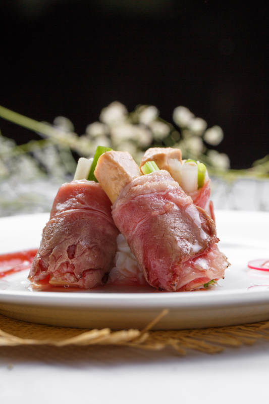 白色圆盘装的法式鹅肝牛肉卷摆放在草垫上图片