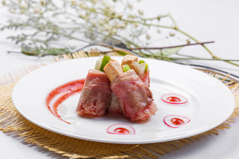 白色圆盘装的法式鹅肝牛肉卷摆放在草垫上图片