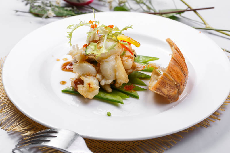 香辣铁板煎龙虾尾肉摆放在草垫上图片