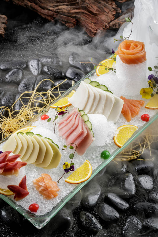刺身拼摆放在干冰缭绕的黑色鹅卵石上图片