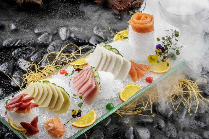 刺身拼摆放在干冰缭绕的黑色鹅卵石上图片