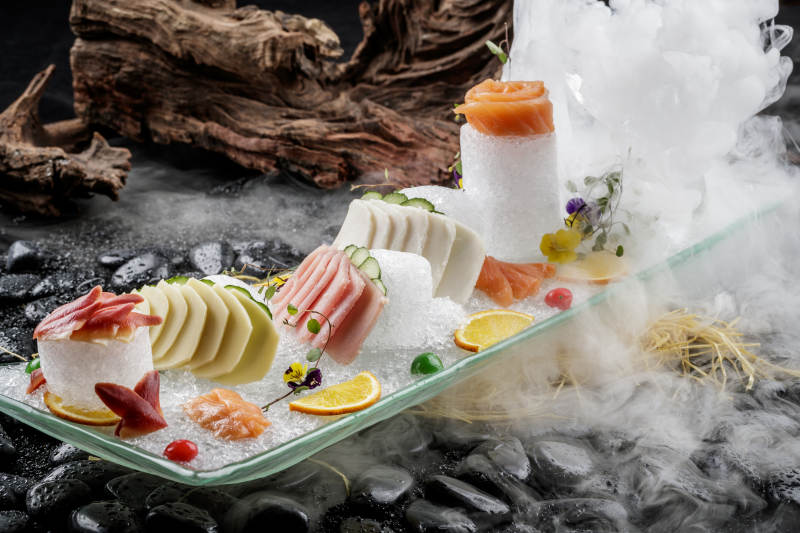 刺身拼摆放在干冰缭绕的黑色鹅卵石上图片