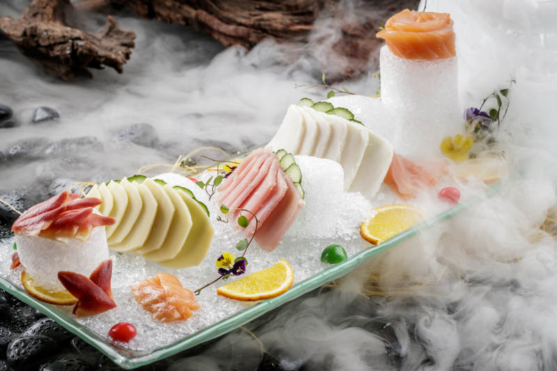 刺身拼摆放在干冰缭绕的黑色鹅卵石上图片