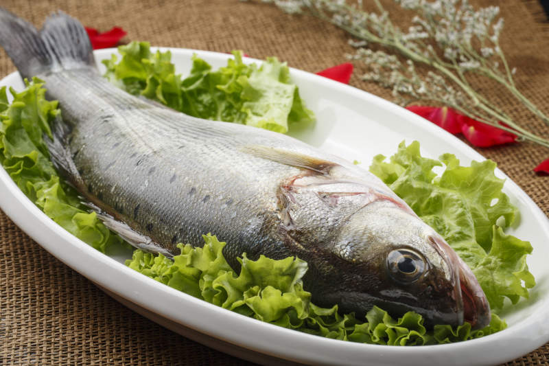 白色椭圆瓷盘装的新鲜海鲈鱼图片