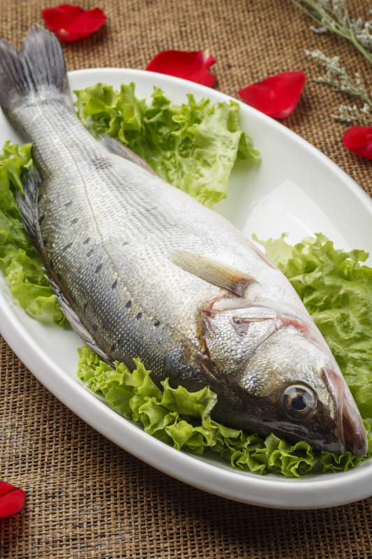 白色椭圆瓷盘装的新鲜海鲈鱼图片