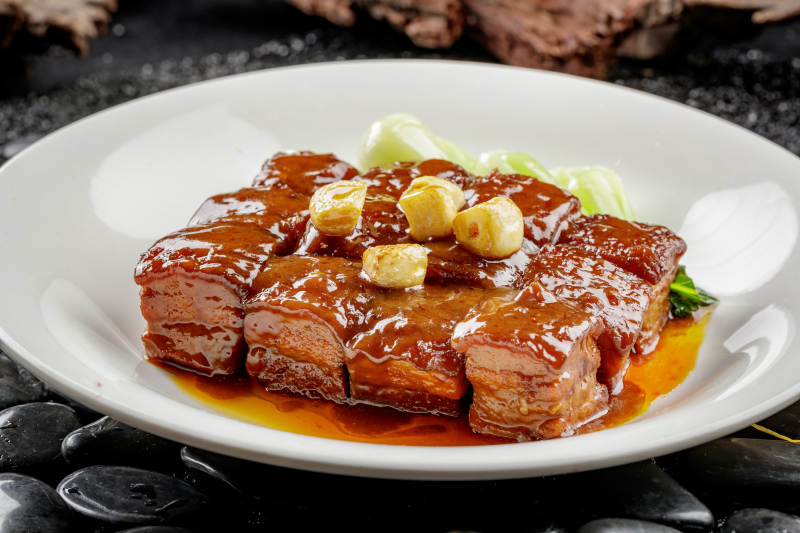 白色圆盘装的毛氏红烧肉摆放在黑色鹅卵石上图片