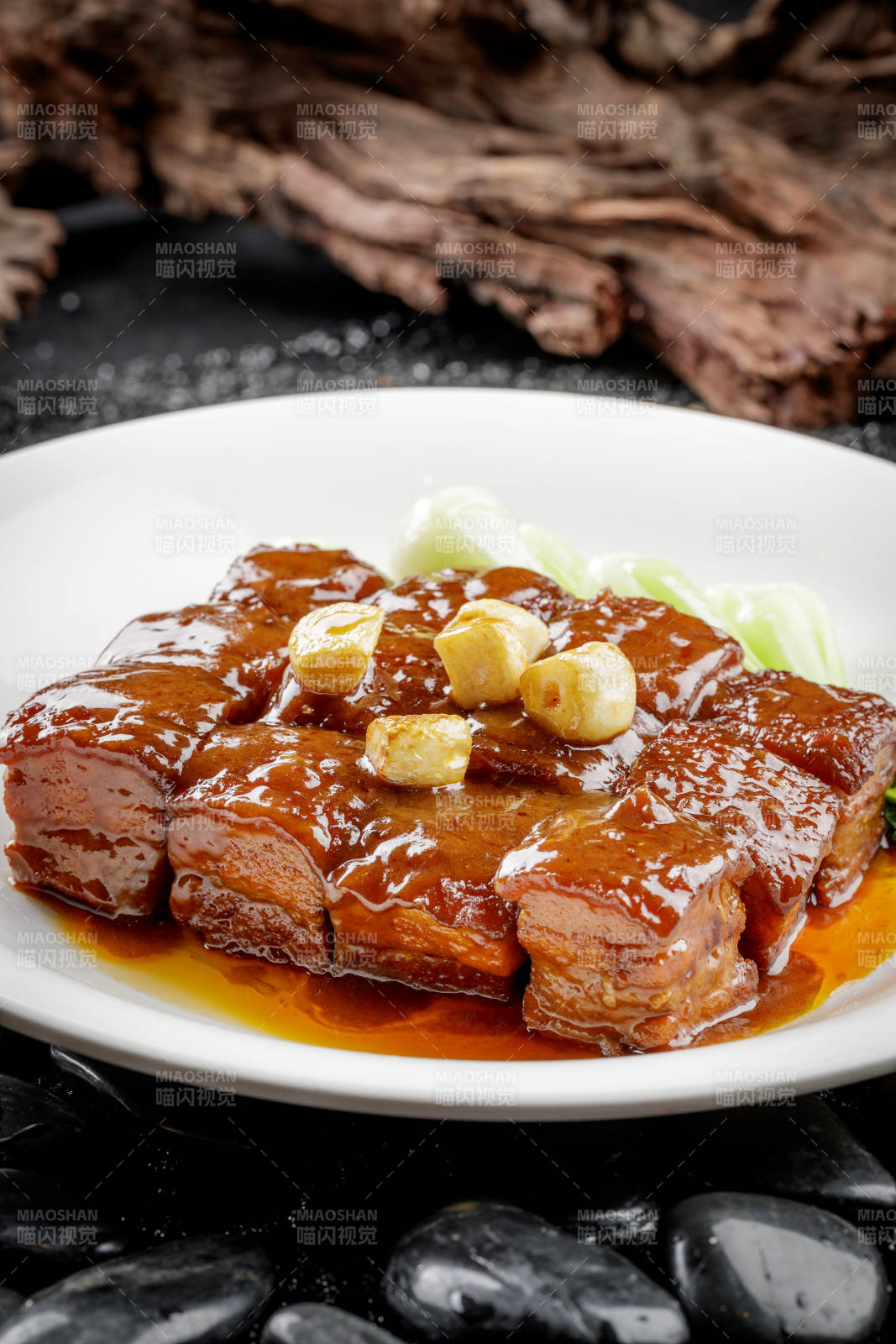 白色圆盘装的毛氏红烧肉摆放在黑色鹅卵石上图片