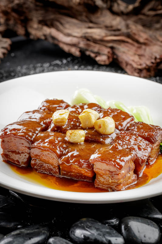 白色圆盘装的毛氏红烧肉摆放在黑色鹅卵石上图片