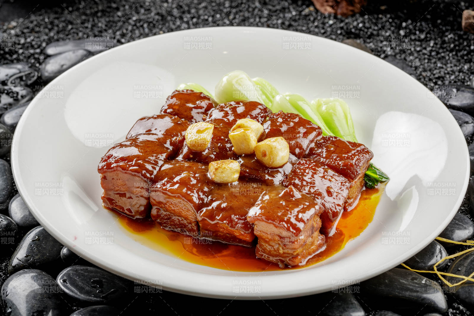 白色圆盘装的毛氏红烧肉摆放在黑色鹅卵石上图片