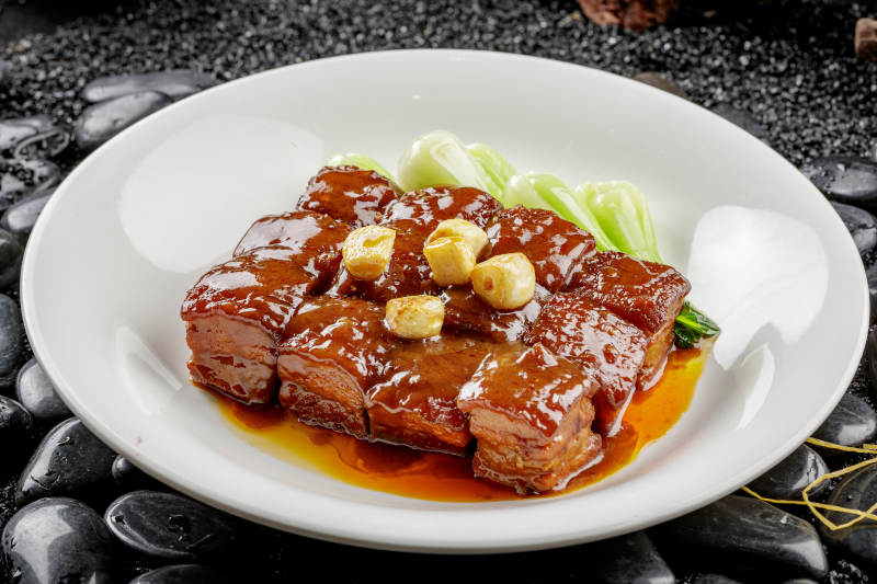 白色圆盘装的毛氏红烧肉摆放在黑色鹅卵石上图片