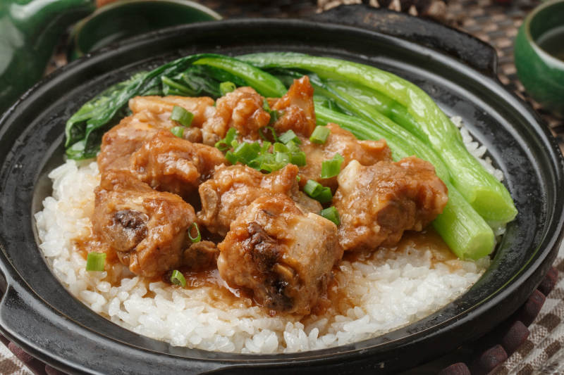 黑色砂锅装的排骨芥蓝煲仔饭摆放在餐布上图片